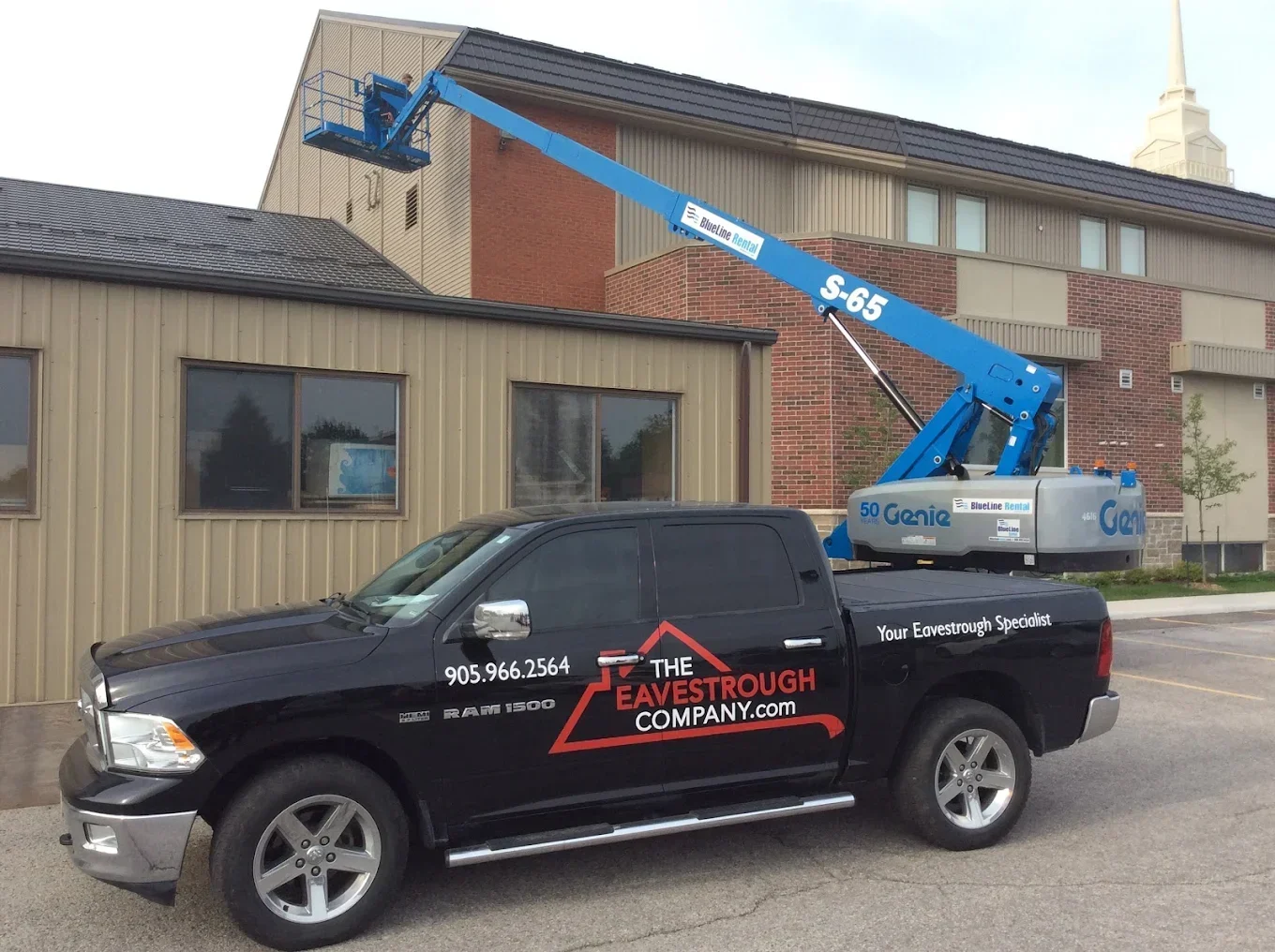 A view of a company truck with a lift holding a worker installing new eavestroughs on a home, part of The Eavestrough Company's exterior renovation photo gallery