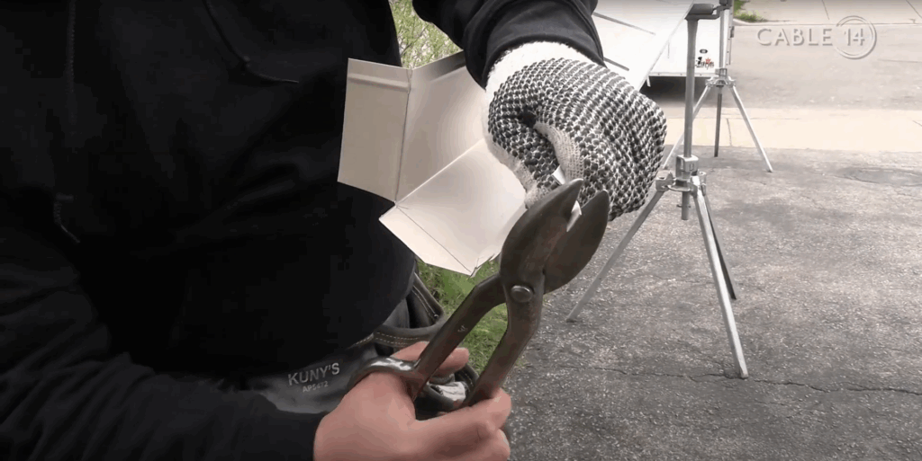 An aluminum gutter corner being cut with tin scissors
